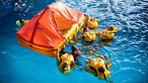 Lifeboat crew members are having training in the sea survival pool with a yellow and orange raft.