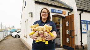 A female RNLI volunteer is standing outside an RNLI shop and smiling
