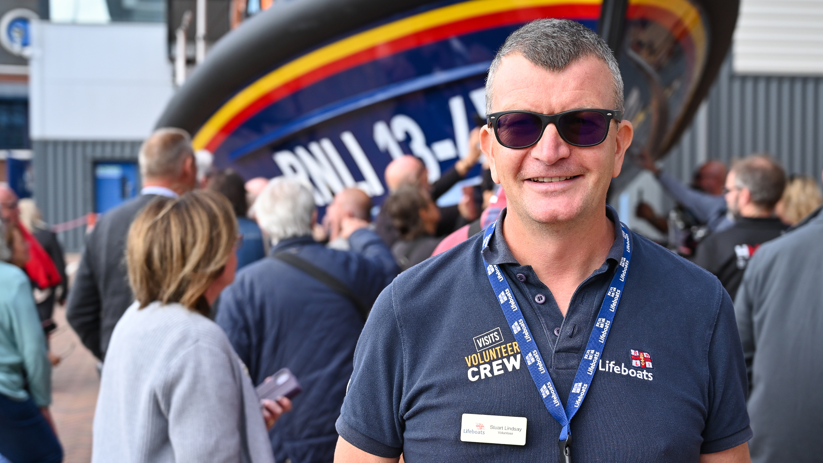 An RNLI visits volunteer at a Launch a Memory event, with a crowd of people viewing the Anstruther lifeboat in the background.