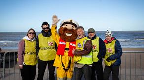 Five people in yellow RNLI Lifeboats vests gather round another figure dressed as the Stormy Stan mascot.