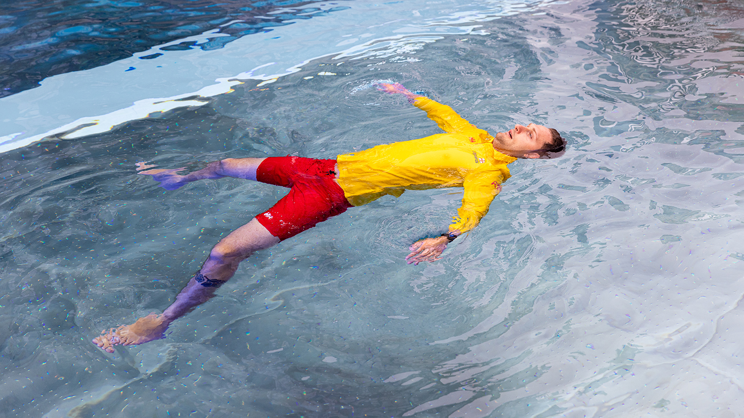 An RNLI lifeguard fully clothed floating in a starfish position in a pool