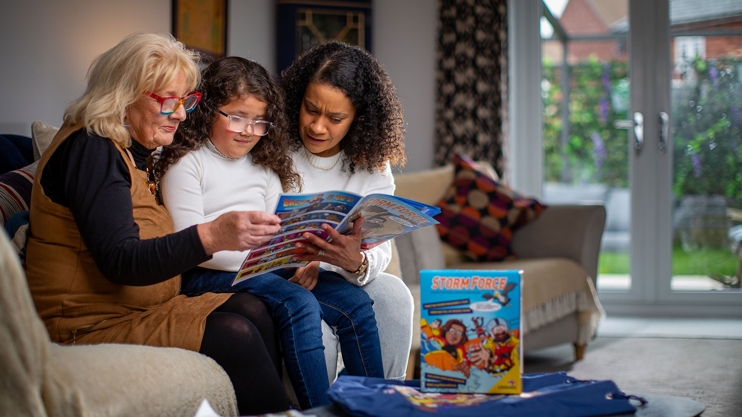 Two adults sat either side of a child reading an RNLI Storm Force magazine