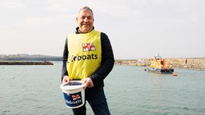 RNLI Volunteer standing by the sea holding a collection bucket