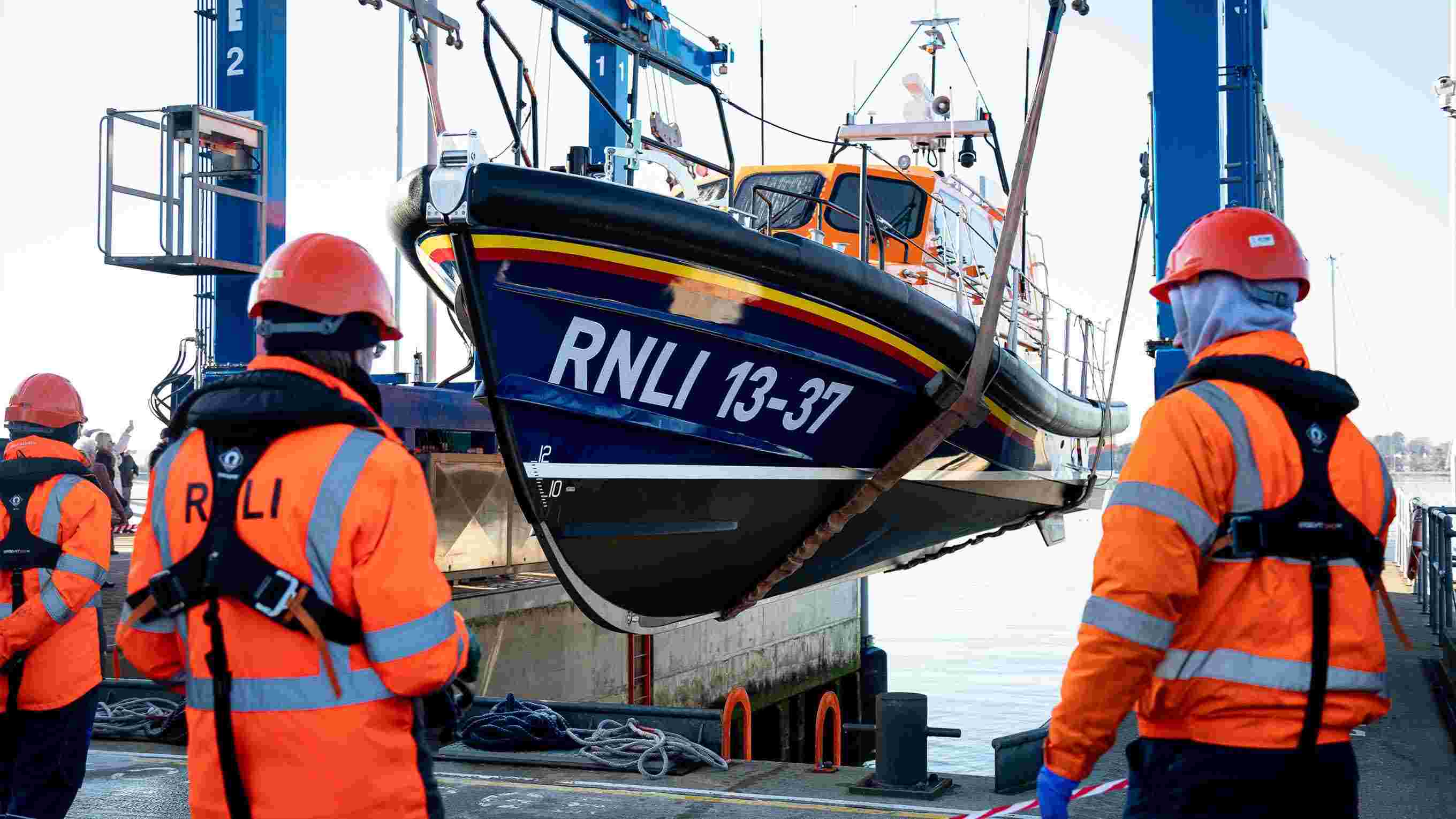 Three lifeboat engineers watch a Shannon class being lowered into the water by a crane