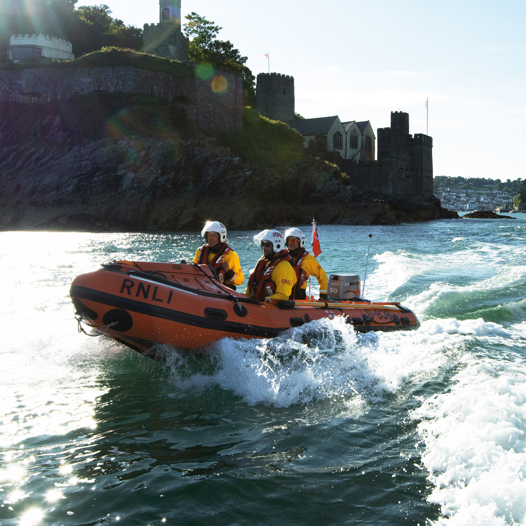 Three crew members aboard Dart RNLI's D class lifeboat on a bright, sunny day