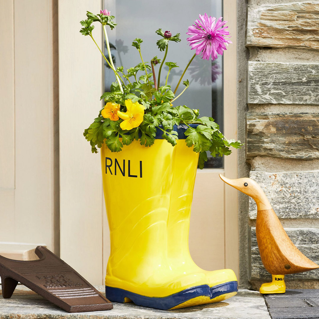 A ceramic planter in the shape of RNLI yellow wellies, with flowers blooming from the top of the planter