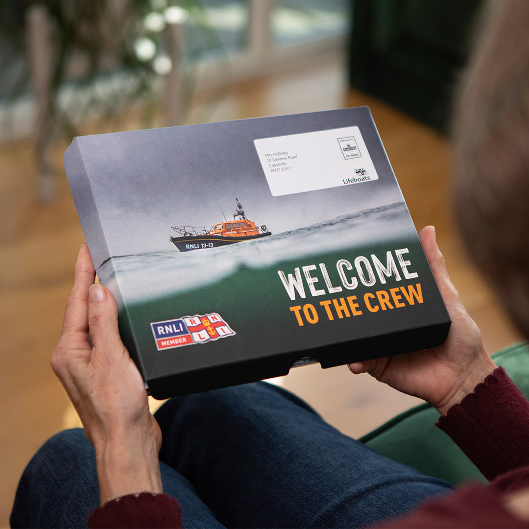 A woman sitting on a sofa and looking through the RNLI's membership pack