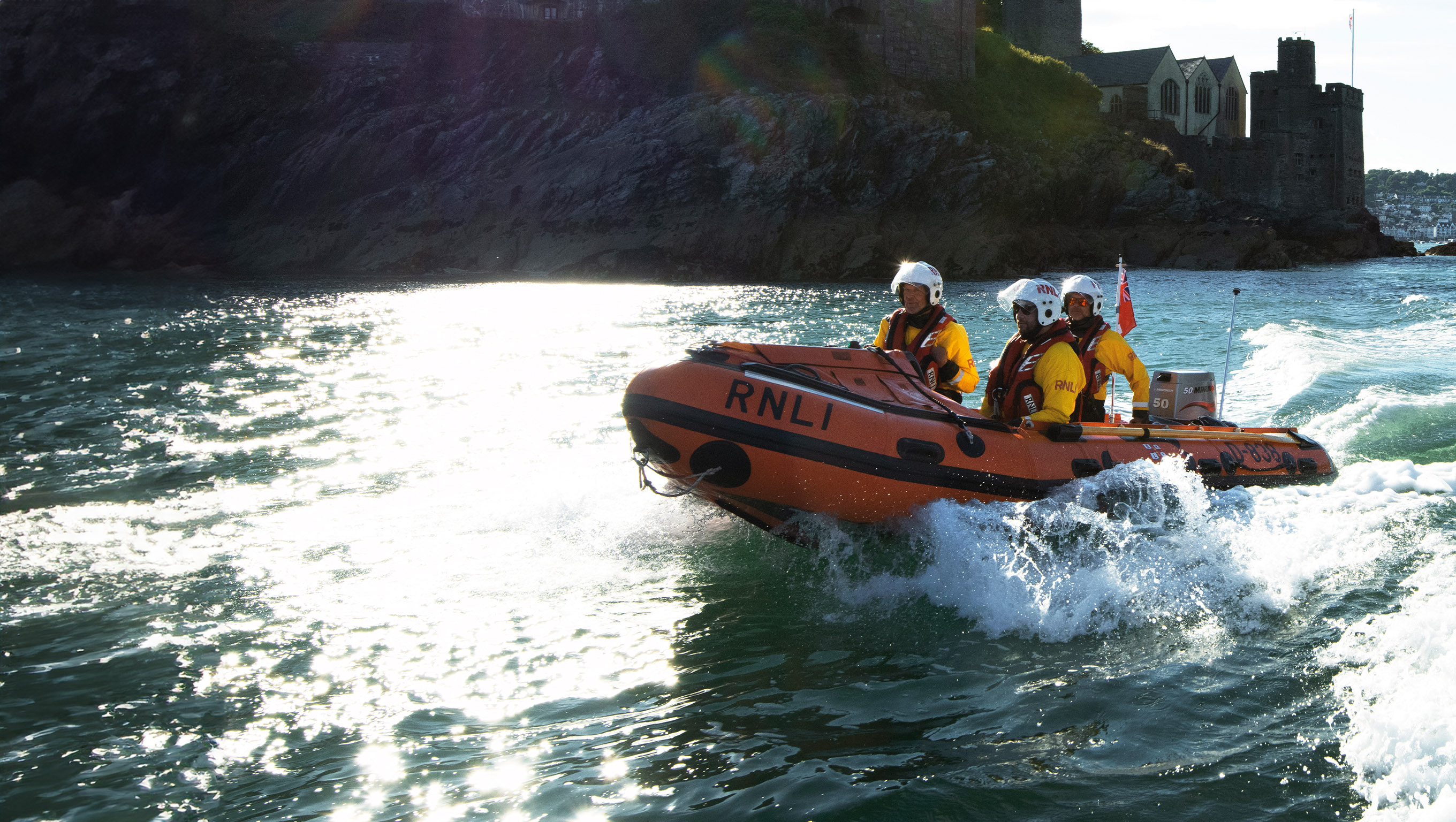 Three crew members aboard Dartmouth's D class lifeboat on a bright, sunny day