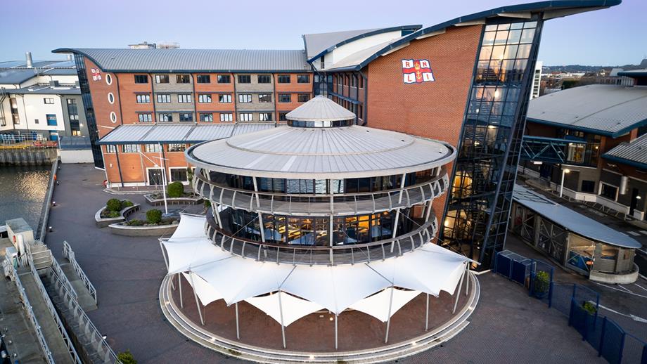 An aerial drone shot of the RNLI College at dusk. Outdoor areas include the sea terrace and pontoon. The round building houses the Harbour View Suite on the top floor. The building behind houses the Waterfront Suite on the ground floor and guest bedrooms.