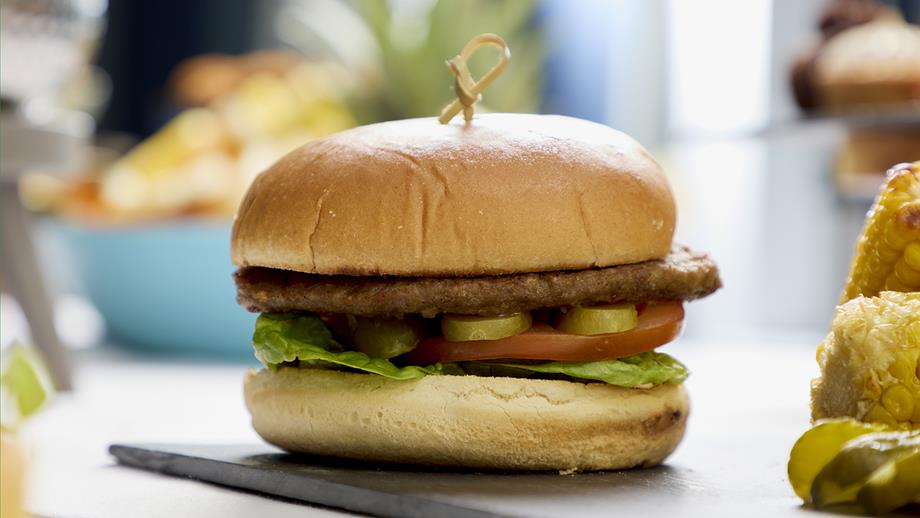 A close-up shot of a burger in a bun with lettuce, tomatoes and gherkins on a black slate serving dish.
