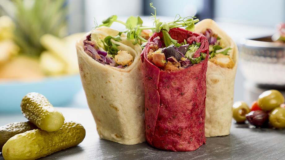 A selection of filled wraps alongside gherkins and olives on a black slate serving dish.