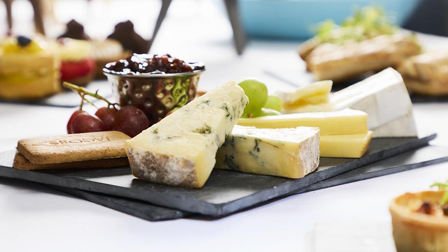 A selection of cheeses with some crackers, grapes and chutney on a black slate serving dish.