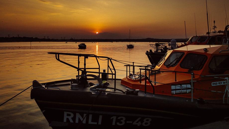 Sunset over Holes Bay at the RNLI College. A Shannon class all-weather lifeboat is moored against the pontoon.